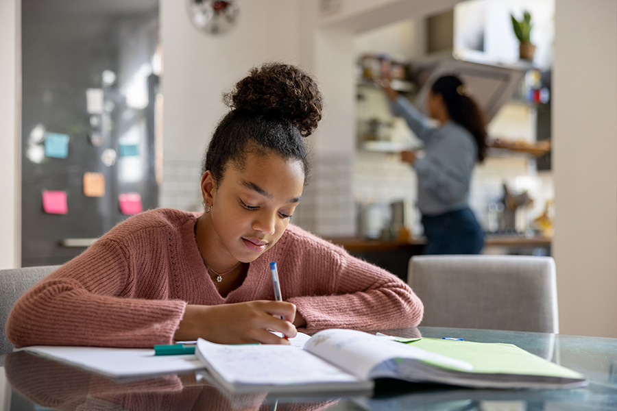 child doing homework in the kitchen with mother putting away dishes. homework strategies for children with ADHD