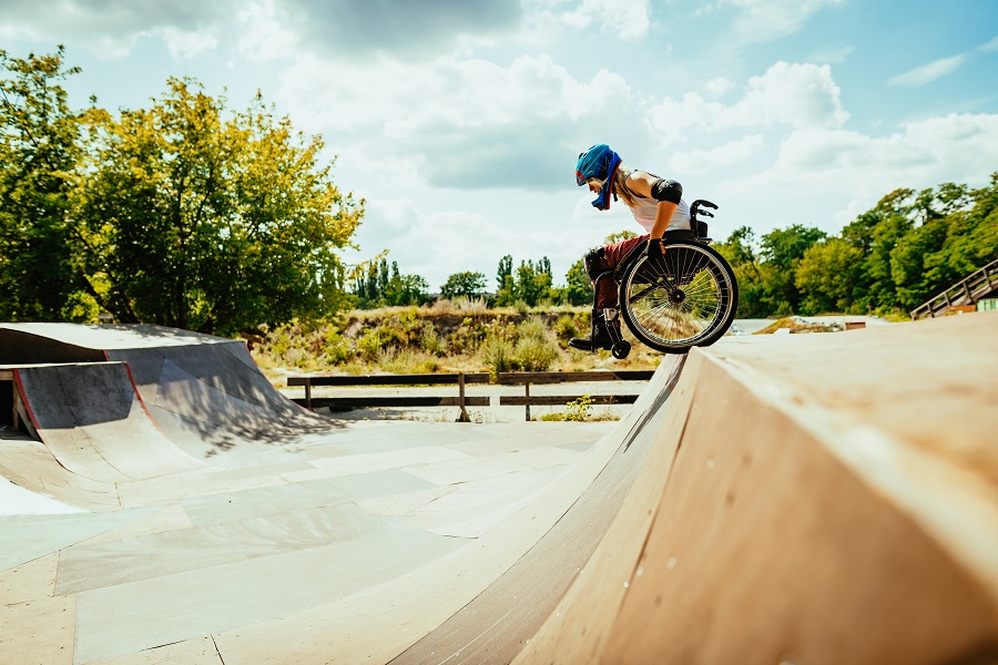 Disabled millennial woman in wheelchair rolls down the hills in skate park