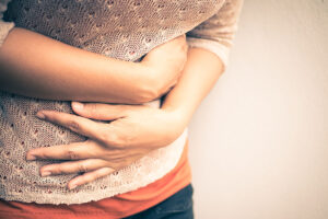 colonoscopies for early detection and screening. Close up of a young woman holding gut, hunched over and clearly in pain