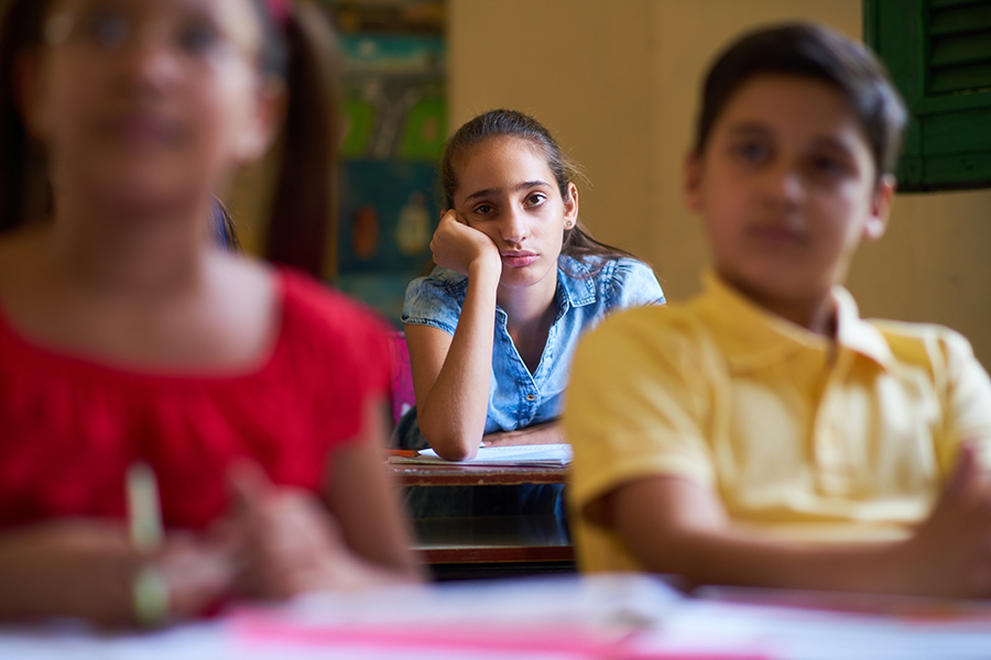 anxious girl sitting in the back of a middle school classroom, with her head in her hand. Managing post Covid long anxiety in our children