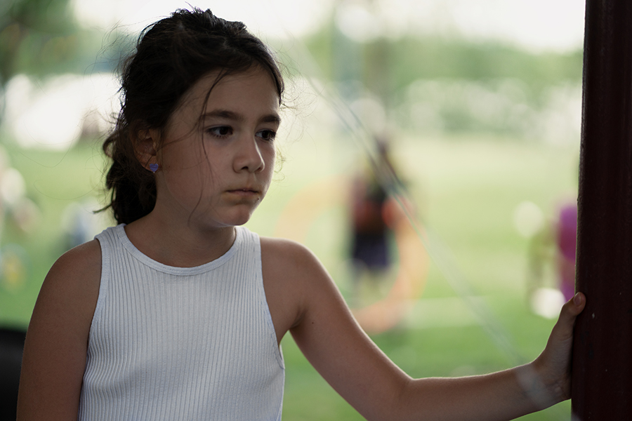 summertime anxiety in children. Anxious child looking sadly off in the distance while children play in the grass behind her.