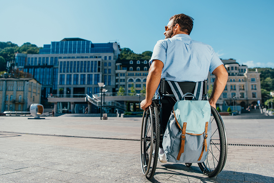 back view of man using wheelchair with bag on street