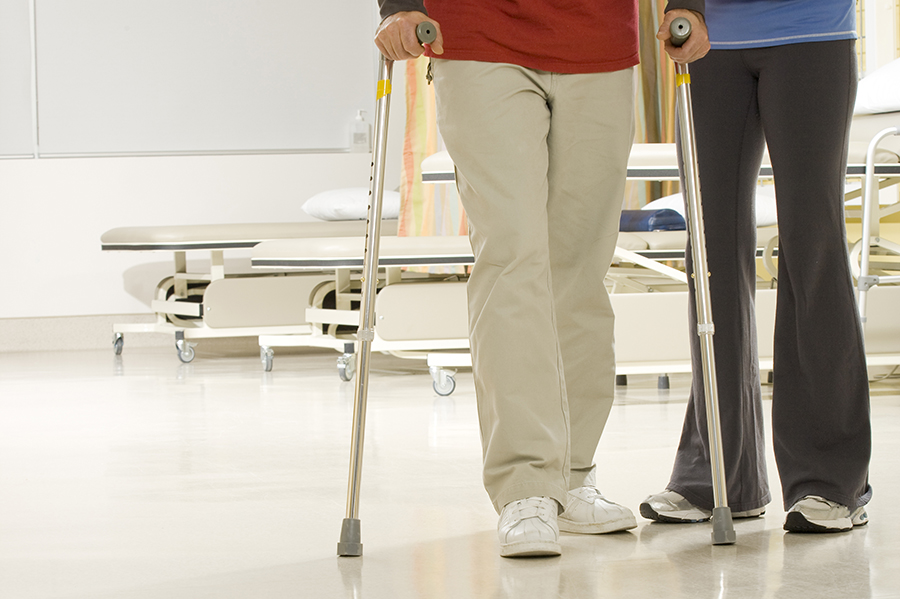 Woman helping man walk on crutches in hospital