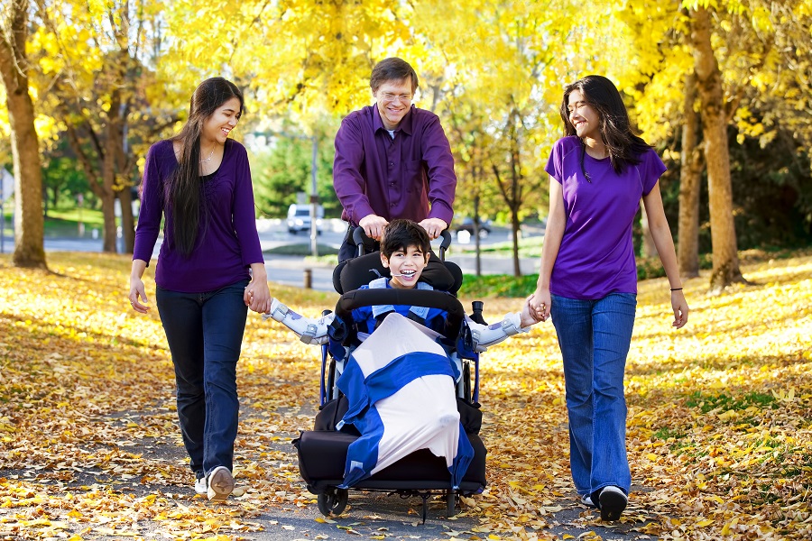 Family with disabled child in wheelchair walking among autumn leaves