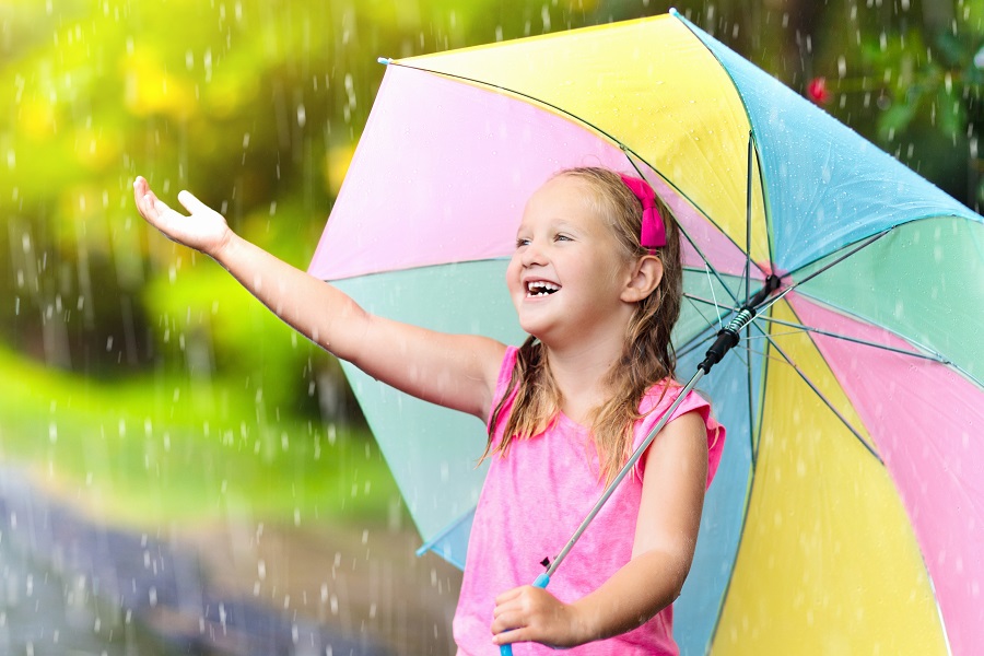 Kid with umbrella playing in summer rain.